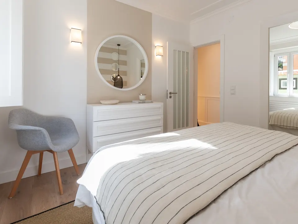 Segundo quarto com cómoda, cadeira e espelho redondo
